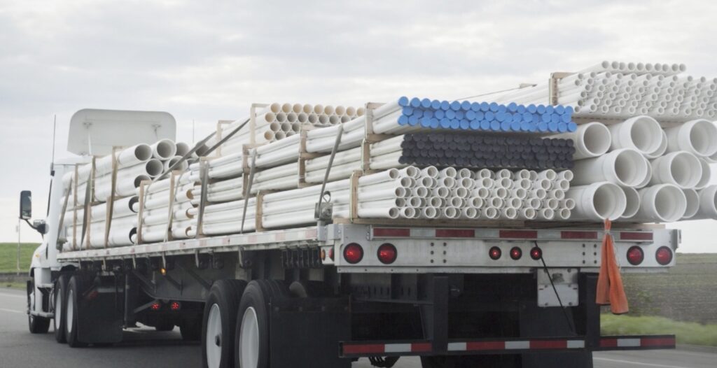 Image of a flatbed shipment hauling large, plastic piping. 