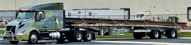 Gray and green truck flatbed transporting a long steel beam