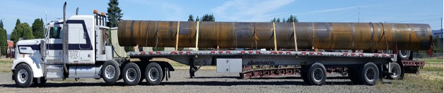 White truck with flatbed trailer pulling large steel pipe