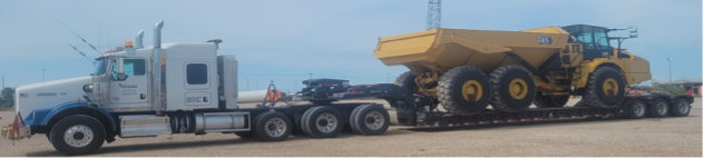 White truck with a double drop hauling heavy equipment shipping