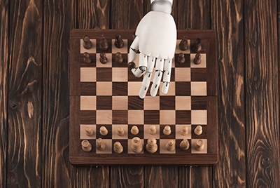 An aerial shot of a robot hand, moving a chess piece while playing chess on a wooden game board.