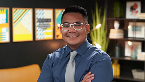 Photo of Nikko Navarro, Director of Marketing at Trinity, a smiling medium-skinned toned man with short black hair, wearing white rimmed glasses, a dark blue collared button down shirt, and a grey-silver tie.  