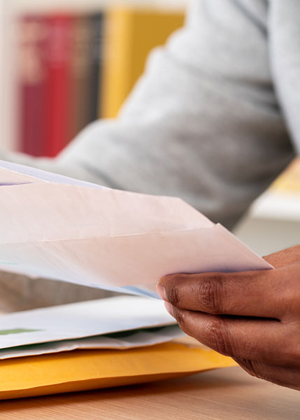Close up of black man hands putting a letter inside an envelope on a desk at home or office