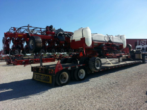 Large red agricultural planter secured on a specialized flatbed trailer, an example of oversized freight supported by Trinity Logistics Sartell, a Minnesota 3PL.
