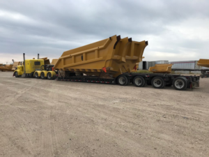 Oversized yellow mining truck bed loaded onto a multi-axle heavy-haul trailer, showcasing specialized freight capabilities supported by Trinity Logistics Sartell, a Minnesota 3PL.
