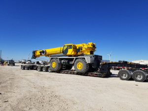Large yellow rough-terrain crane secured to a lowboy trailer for heavy-haul transportation supported by Trinity Logistics Sartell, a Minnesota 3PL.