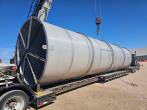 Large cylindrical industrial vessel being lifted by a crane onto a flatbed trailer for specialized transportation supported by Trinity Logistics Sartell, a Minnesota 3PL.